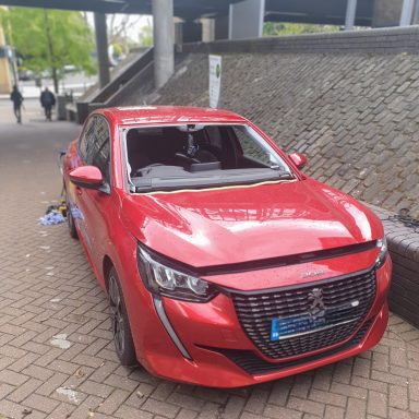 A red car with a broken windshield parked on the road, perfect for Epic Windscreens Mobile Fleet replacement services.