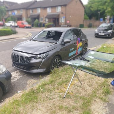 A Peugeot parked on a London roadside, with a Epic Windscreens technician replacing its damaged windscreen.